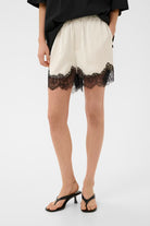 Person wearing white shorts with black lace trim on a white background