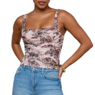 Woman wearing a patterned tank top and blue jeans against a gray background