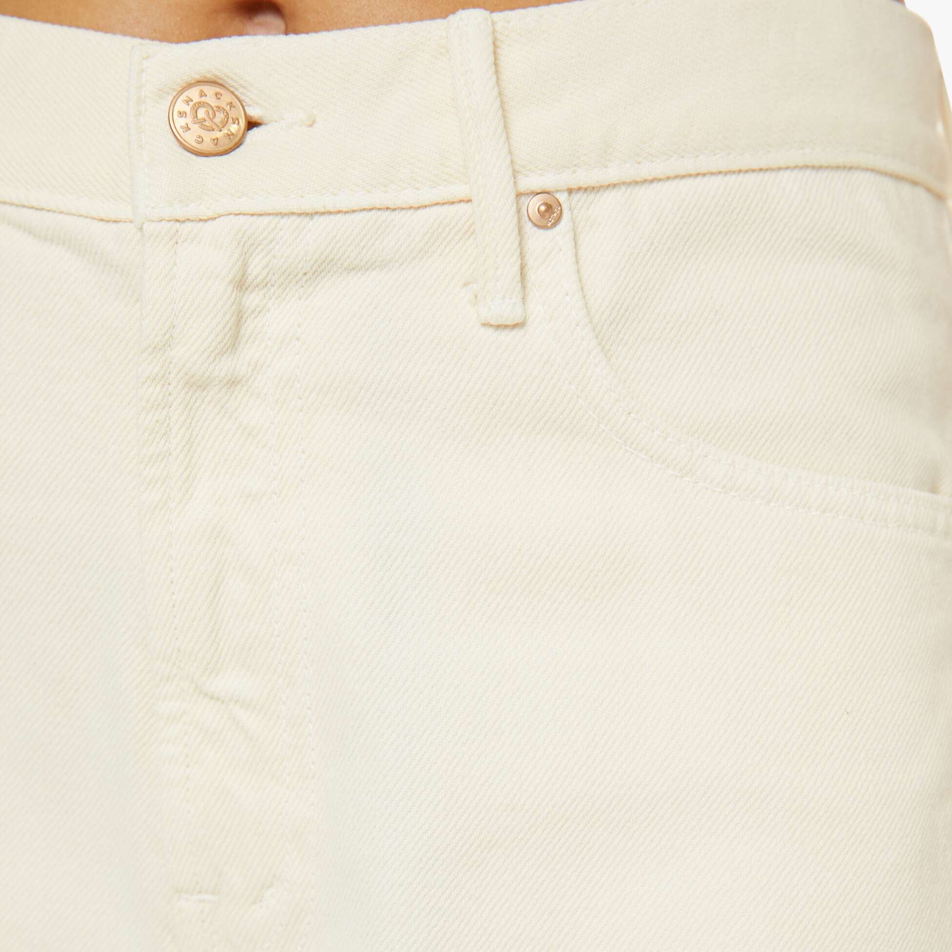 Close-up of beige pants with a brand logo on the button.