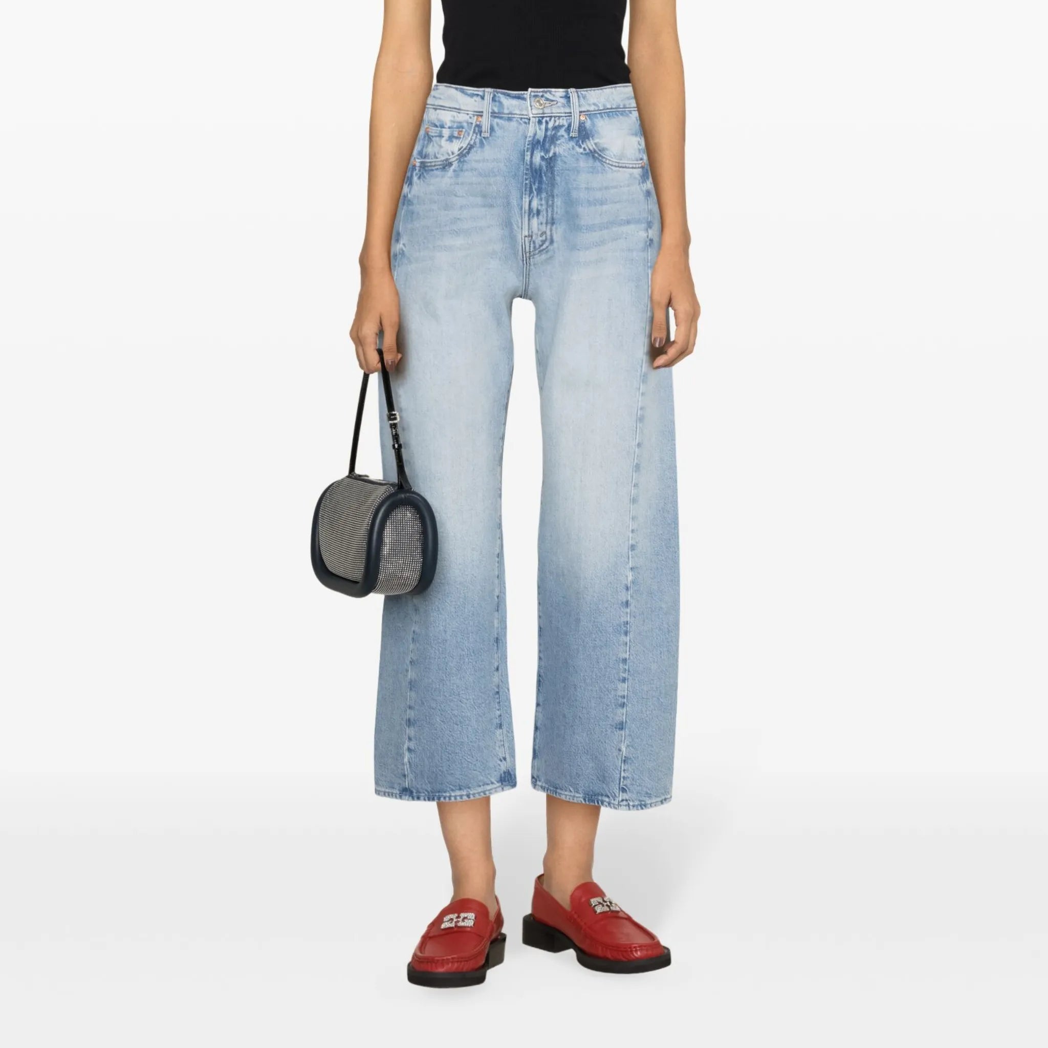 Person wearing a black tank top, light blue jeans, and red shoes on a white background