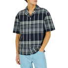 Man wearing a plaid shirt and light blue pants on a white background