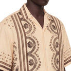 Beige shirt with brown geometric patterns worn by a person on a white background