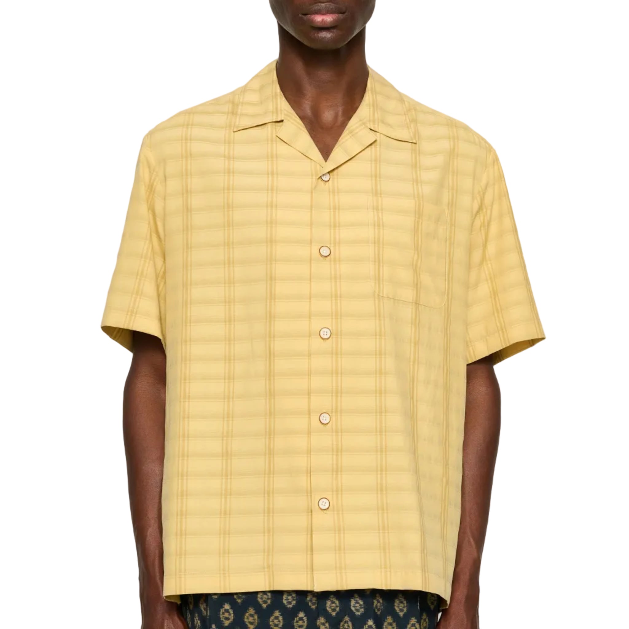 Man wearing a yellow textured shirt with patterned pants on a white background