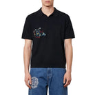 Man wearing a black polo shirt and blue jeans against a white background