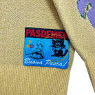 Yellow sweater with a colorful patch featuring text and graphics on a white background