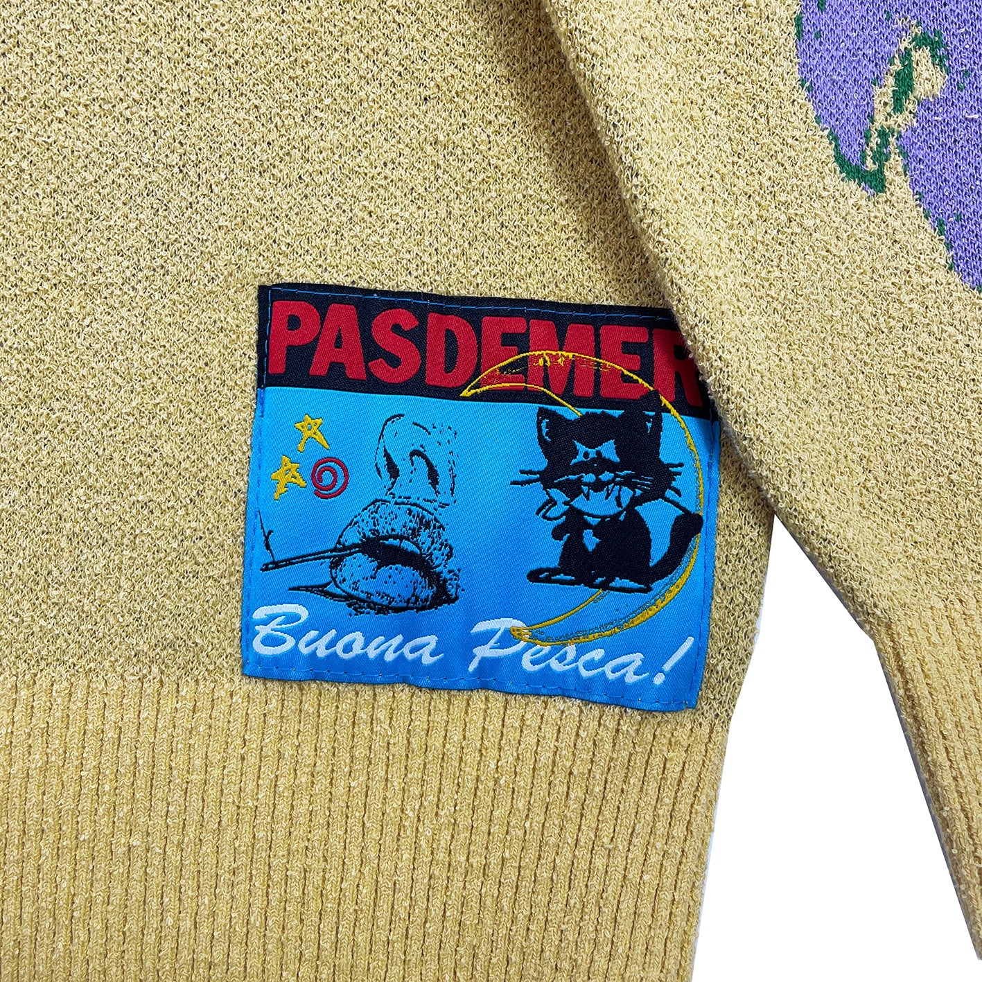 Yellow sweater with a colorful patch featuring text and graphics on a white background
