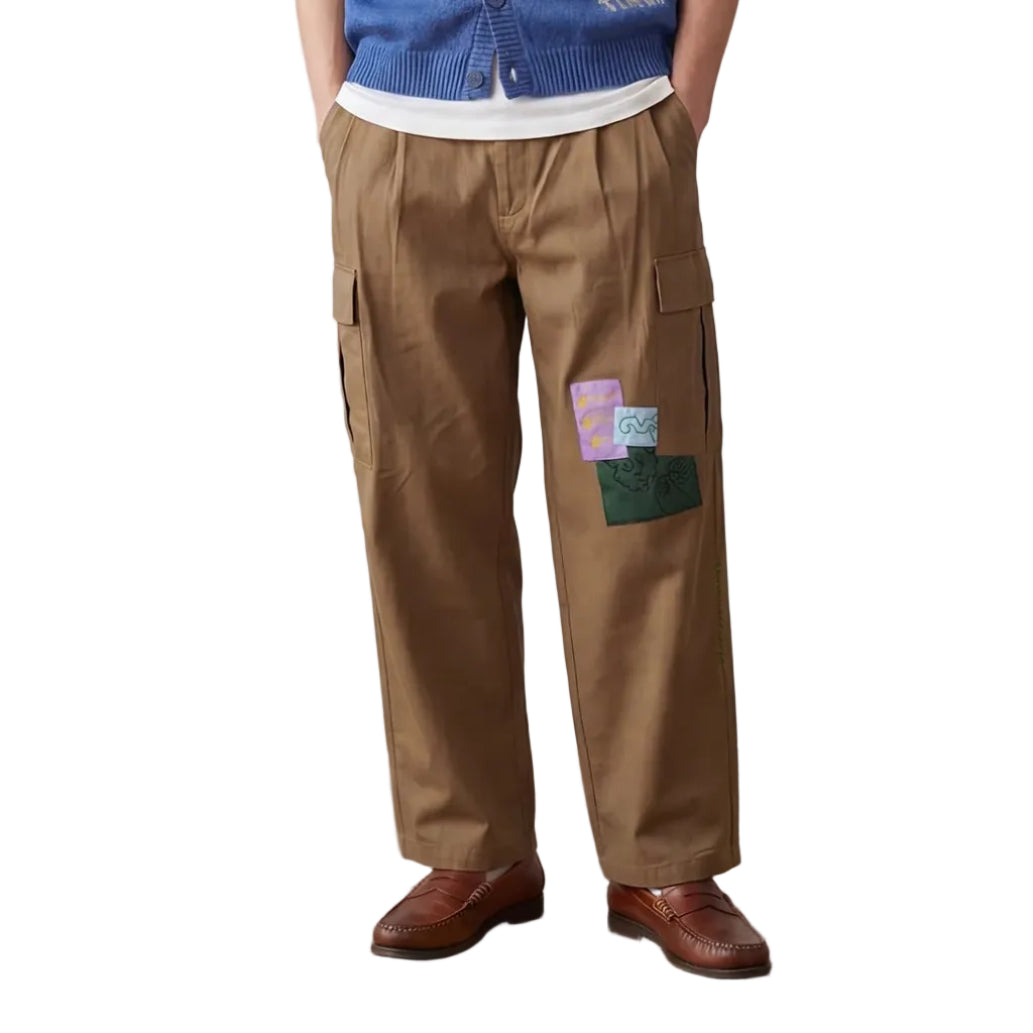 Man wearing a blue vest with white patterns, white shirt, brown pants, and brown shoes on a plain background.