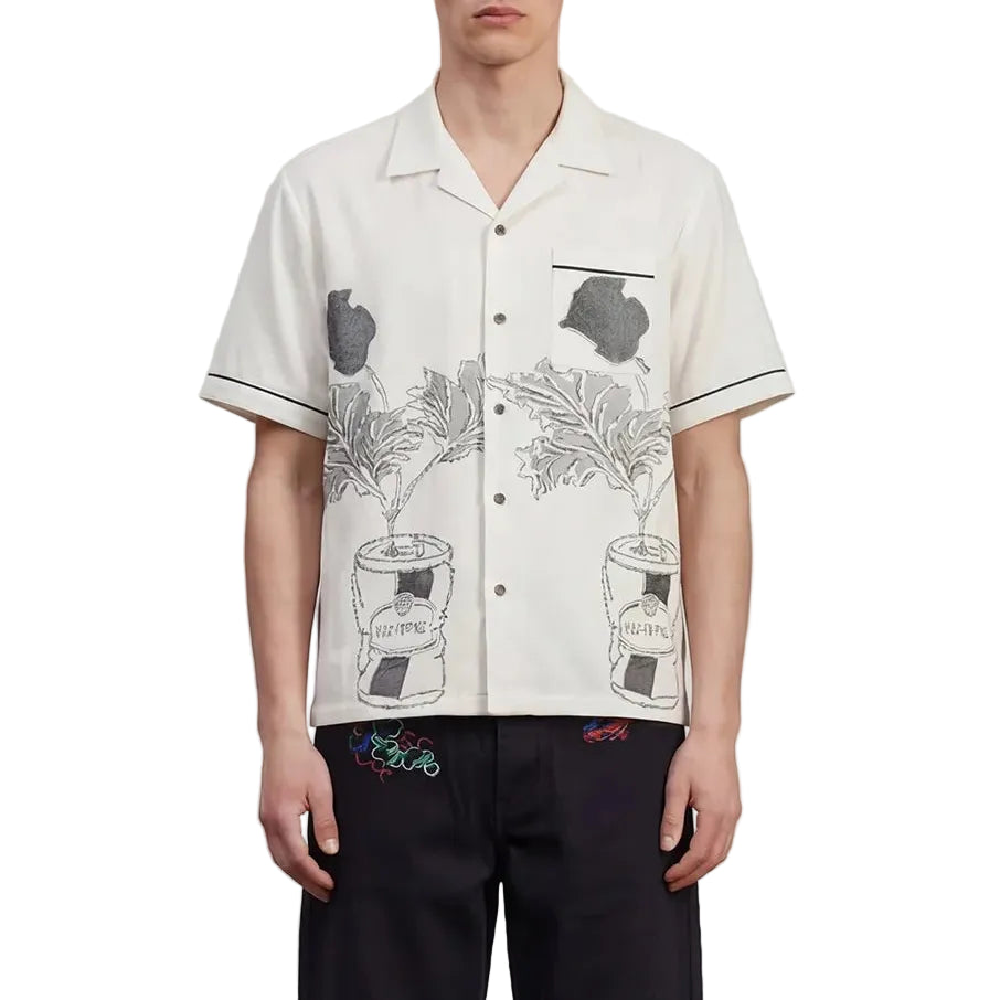 Man wearing a white patterned shirt and black pants standing against a plain background