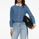A model wearing a blue denim shirt with a white collar, light-wash blue jeans, holding a black leather bucket bag against a plain white background.