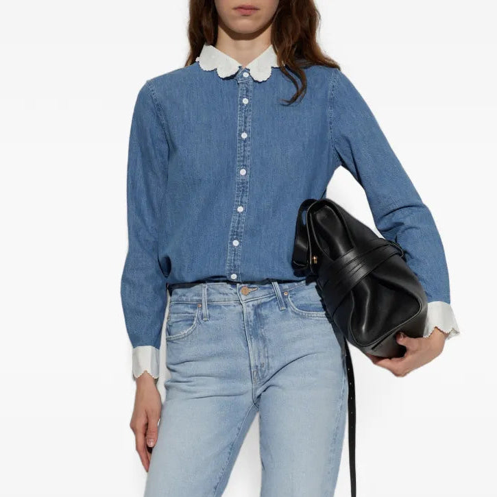 A model wearing a blue denim shirt with a white collar, light-wash blue jeans, holding a black leather bucket bag against a plain white background.