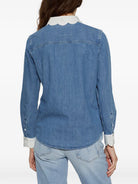 A woman shown from the back wearing a medium-wash blue denim shirt with a contrasting white scalloped collar and white rolled cuffs, paired with light-wash jeans against a plain white background.