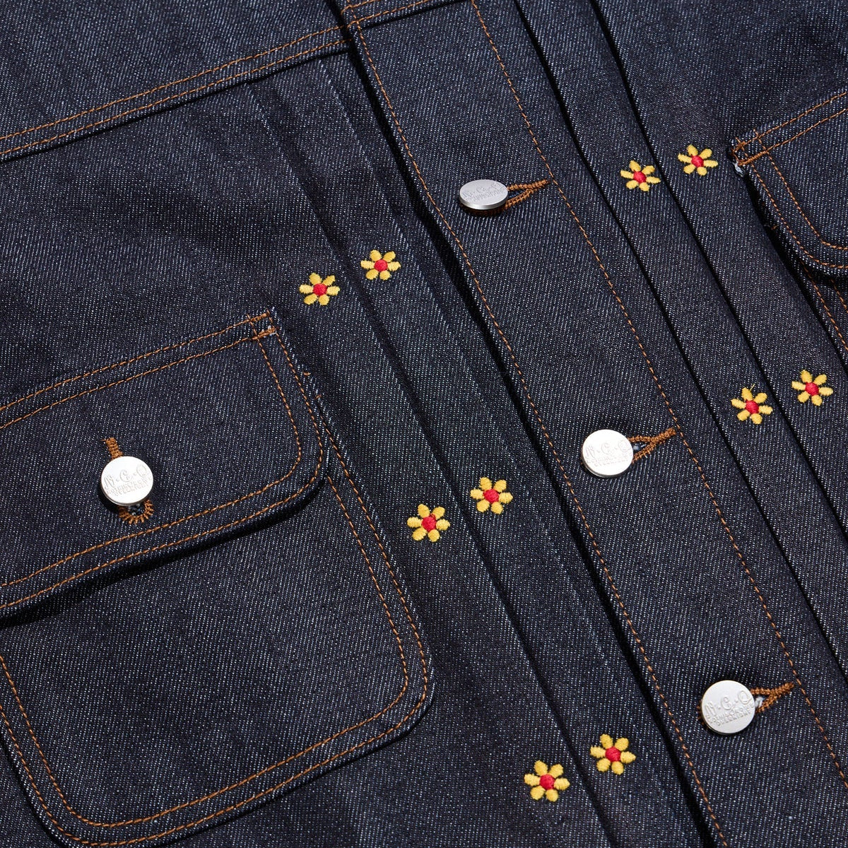 Close-up of a denim jacket with floral embroidery and buttons.
