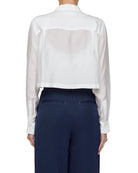 Person wearing a white sheer blouse over a navy suit on a plain background
