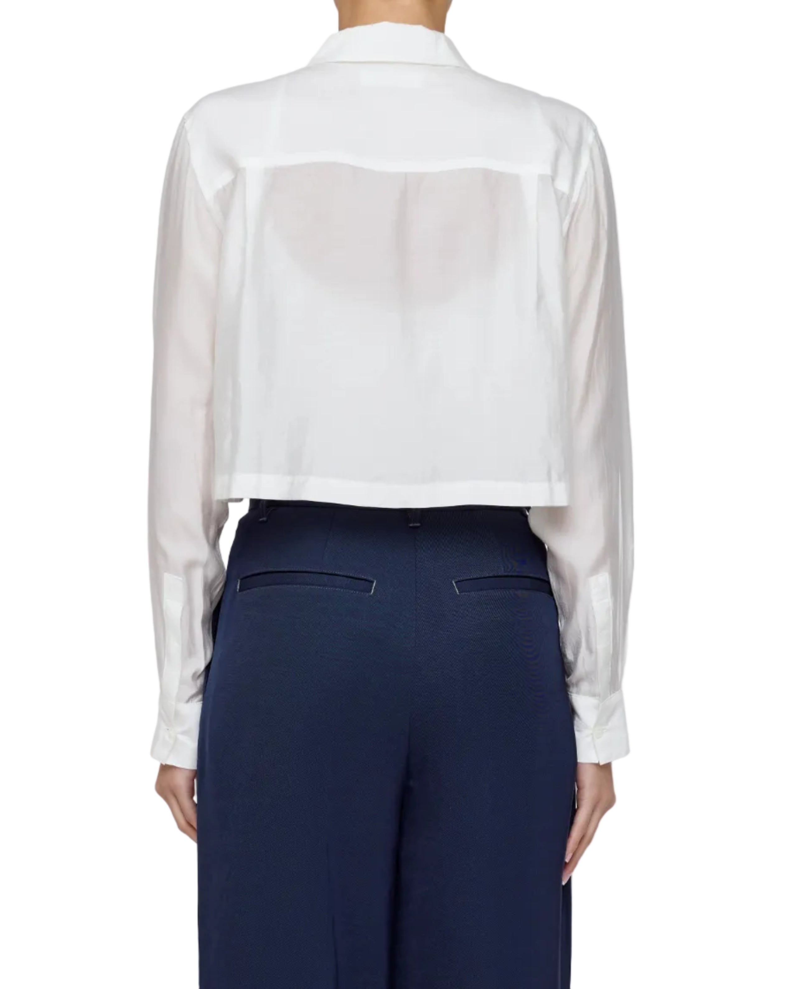 Person wearing a white sheer blouse over a navy suit on a plain background