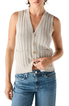 Woman wearing a beige knitted vest over a white shirt with blue jeans on a white background
