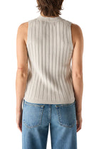 Person wearing a grey ribbed sleeveless sweater and blue jeans on a white background