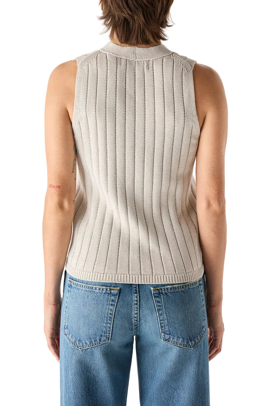 Person wearing a grey ribbed sleeveless sweater and blue jeans on a white background