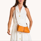Model in a white dress with a light brown leather cross body bag with silver accents on a white background