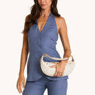 Model in a blue outfit with a Cream leather bag with gold accents on a white background