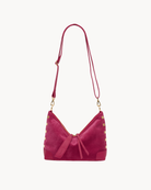 Pink suede cross body bag with gold accents on a white background