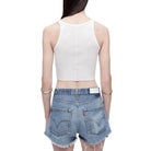 Back view of a model in a white tank top and denim shorts on a white background