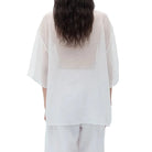 Back view of a person wearing an oversized sheer white t-shirt with wide-leg pants on a white background