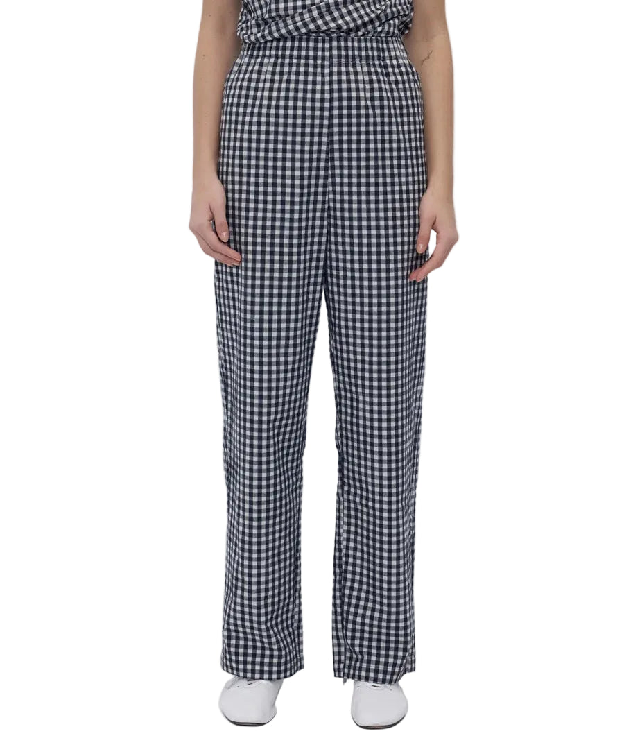 A model wearing a black and white gingham checkered outfit with wide-leg trousers, paired with white shoes, against a plain white background.