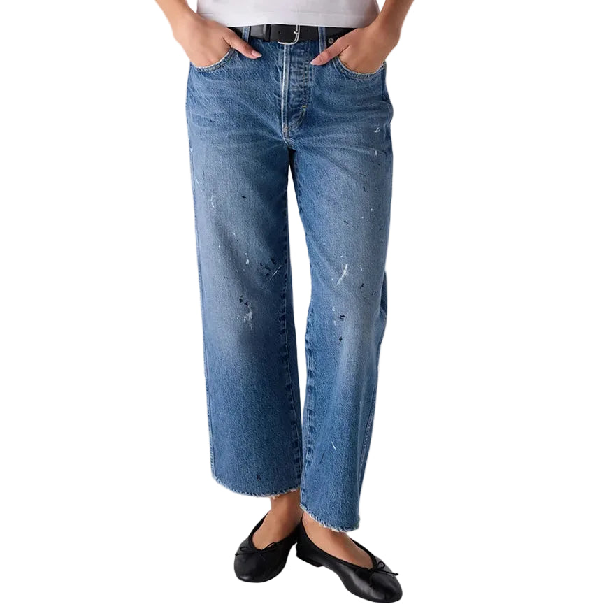 A model wearing a white short-sleeve t-shirt, blue wide-leg cropped jeans with distressed details, a black belt, and black flats, standing against a light gray studio background.