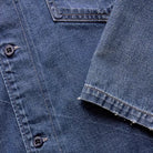 Close-up of a blue denim shirt with buttons and a sleeve.