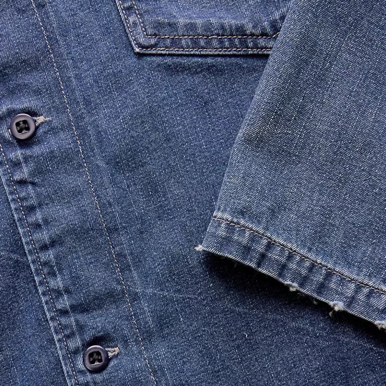 Close-up of a blue denim shirt with buttons and a sleeve.
