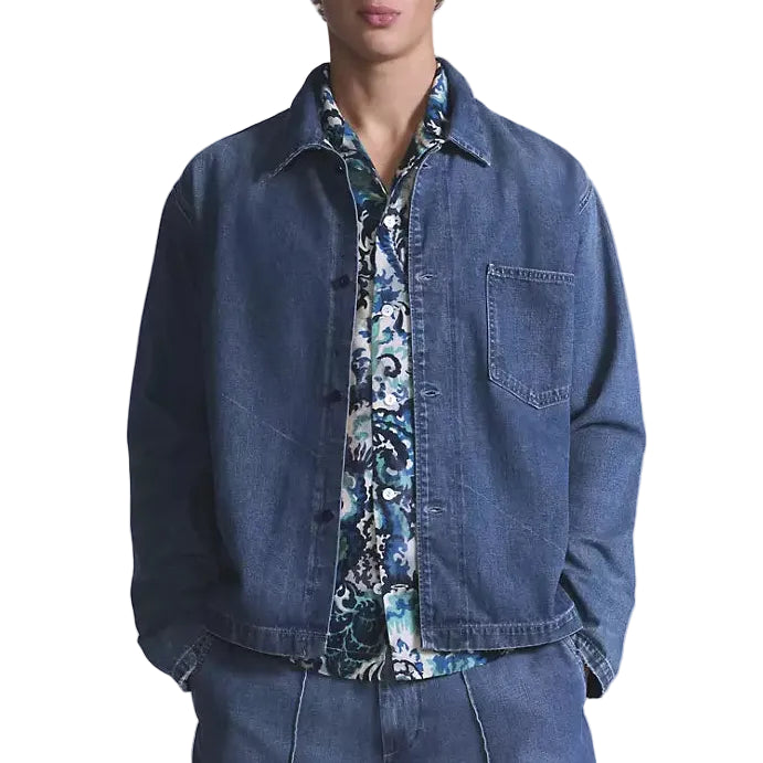 Man wearing a denim jacket over a patterned shirt on a plain background