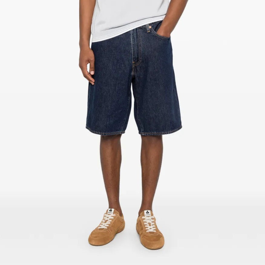 Person wearing a white polo shirt and dark blue denim shorts on a white background