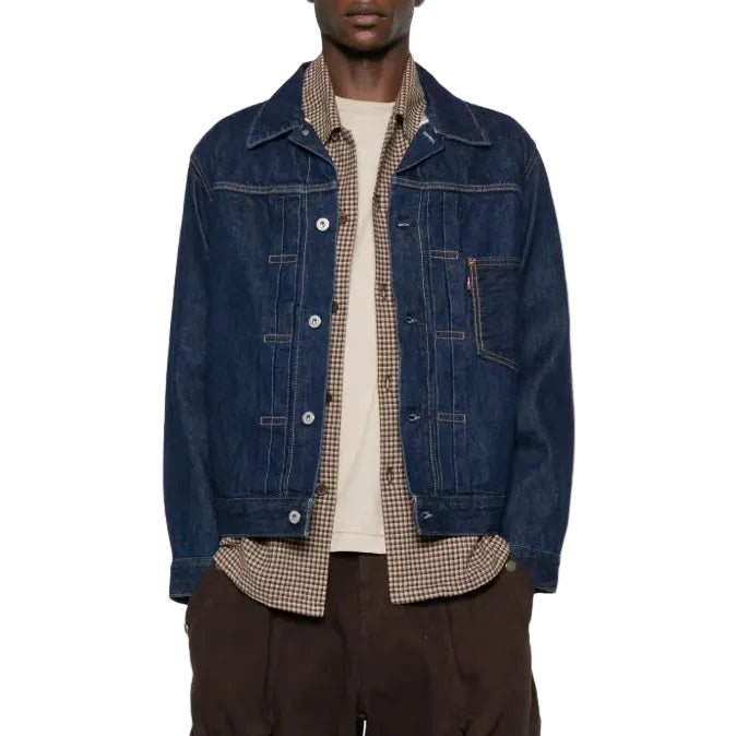 Person wearing a denim jacket, plaid shirt, and dark pants on a white background