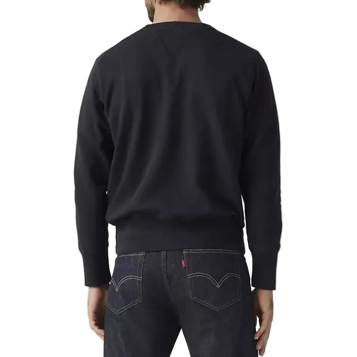 Man wearing a black sweatshirt and dark jeans on a light gray background