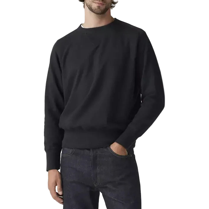 Man wearing a black sweater and dark jeans against a plain background
