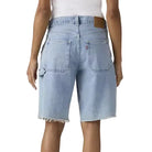 Woman wearing light blue denim shorts and a white top on a plain background
