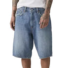 Person wearing a white t-shirt and blue denim shorts on a plain background