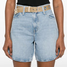 Person wearing light blue denim shorts with a beige belt on a white background