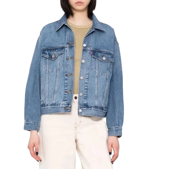Person wearing a blue denim jacket, beige shirt, white pants, and black sneakers on a plain background