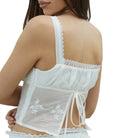 Back view of a model in a white camisole with delicate floral embroidery on a white background