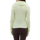 Back view of a woman wearing a light yellow knitted cardigan with a fur collar against a plain background