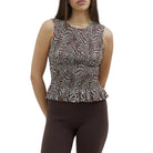 Woman wearing a patterned sleeveless top and brown capri pants on a plain background