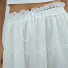 White lace-trimmed skirt with floral embroidery worn by a person.