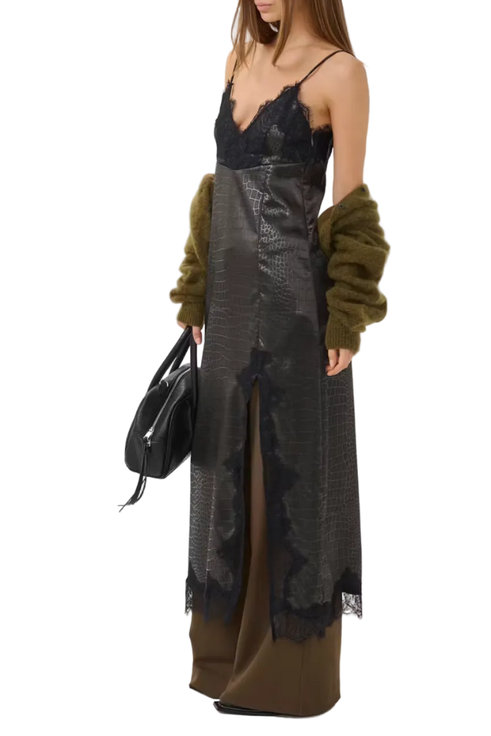 A model is shown from the side wearing a long black lace and textured faux-croc dress with olive green fuzzy cardigan sleeves, brown wide-leg pants, and holding a black handbag against a plain light gray studio background.