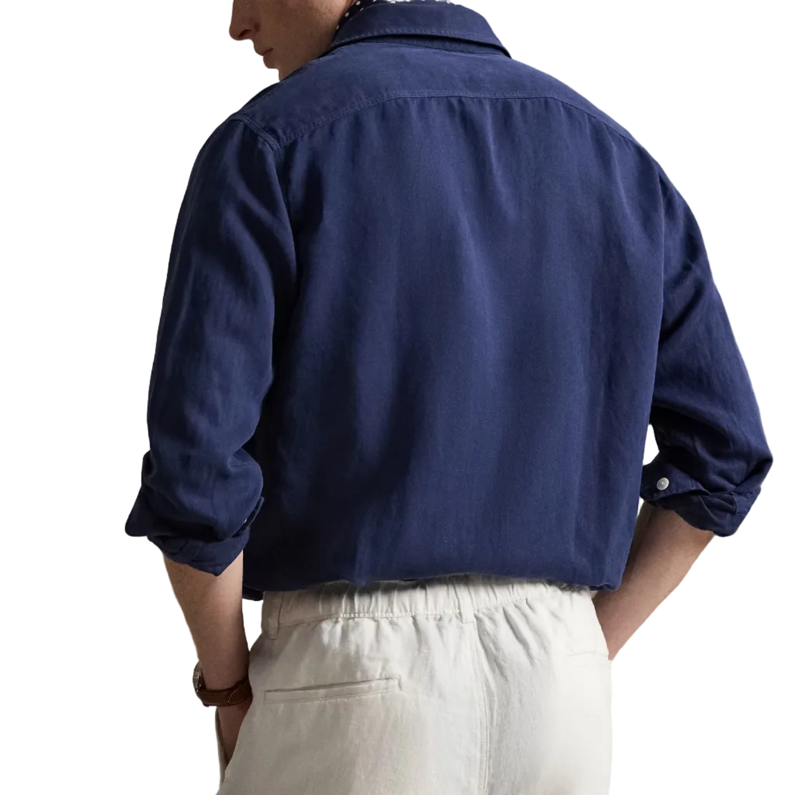 Person wearing a blue shirt and white pants against a beige background