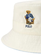 Close up of a white bucket hat with an embroidered bear logo on a white background