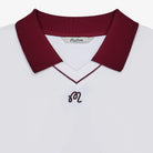 Close-up of a white polo with a maroon collar and logo at the chest on a white background