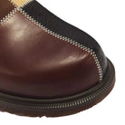 Close-up of a brown leather boot with a black leather toe cap and white zigzag stitching.