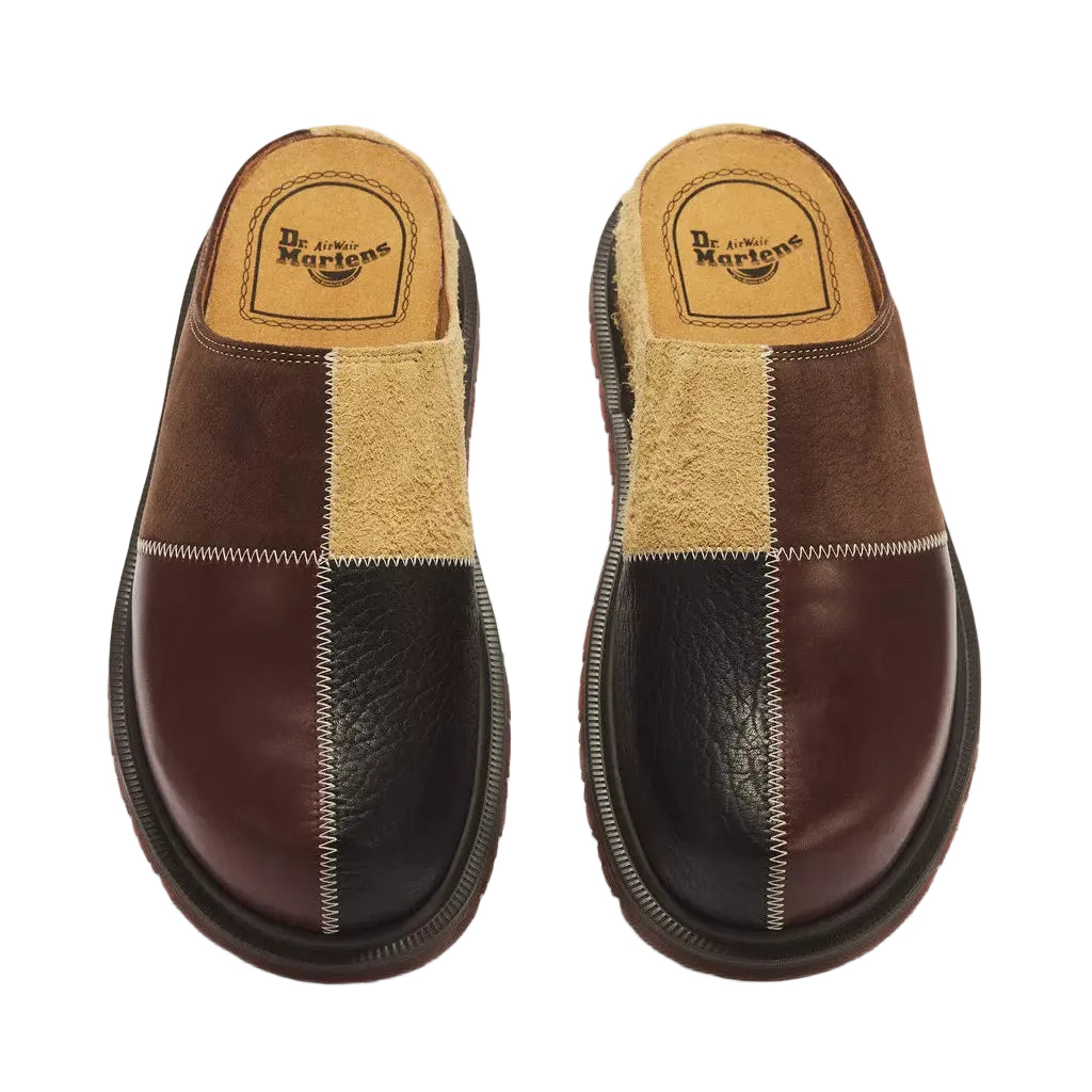 A pair of Dr. Martens slip-on mule shoes with a patchwork design in dark brown leather, burgundy leather, and beige suede, shown from a top-down view on a white background.