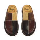 A pair of Dr. Martens slip-on mule shoes with a patchwork design in dark brown leather, burgundy leather, and beige suede, shown from a top-down view on a white background.